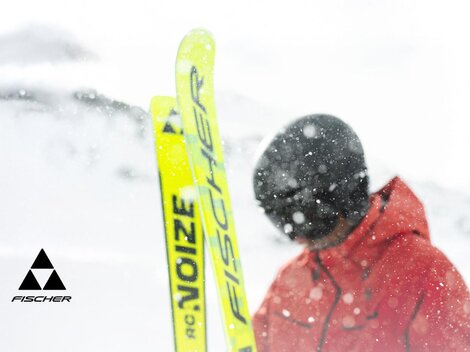 Ein Skifahrer steht im Schnee mit gelben Skiern. Die Umgebung ist winterlich und mit Schnee bedeckt.
