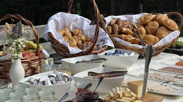 Ein reichhaltiges Frühstücksbuffet mit Körben voller Brötchen und Gebäck. Es gibt verschiedene Marmeladen und viele kleine Leckereien auf einem schön gedeckten Tisch.