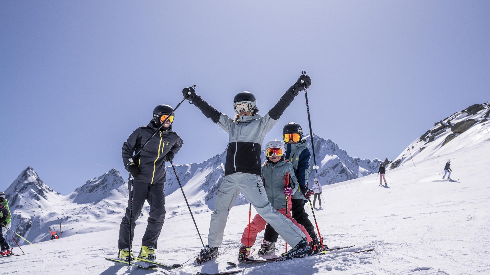 A group of skiers stands on a snow-covered slope in the mountains. The sun is shining and the sky is clear.