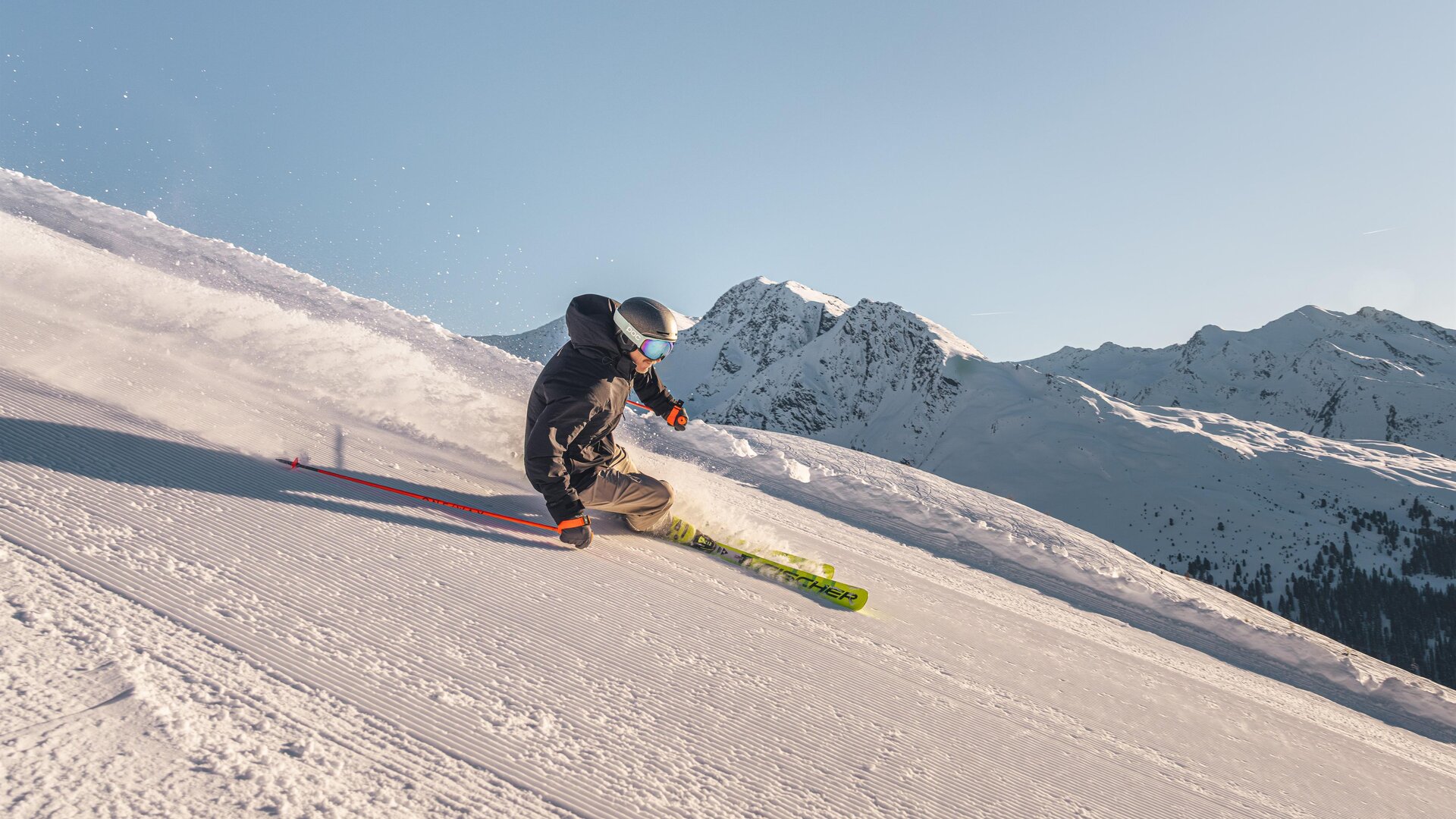 Ein Skifahrer fährt eine verschneite Piste hinunter. im Hintergrund sind schneebedeckte Berge zu sehen.