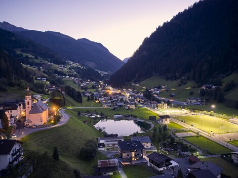 Eine malerische Berglandschaft mit einem ruhigen Tal und einem kleinen Dorf. Die Umgebung ist bei Dämmerung beleuchtet und zeigt eine friedliche Atmosphäre.