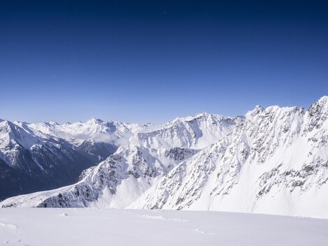 Eine beeindruckende Berglandschaft mit schneebedeckten Gipfeln und klarem blauen Himmel. Die schroffen Felsen und tiefen Täler schaffen eine majestätische Aussicht.
