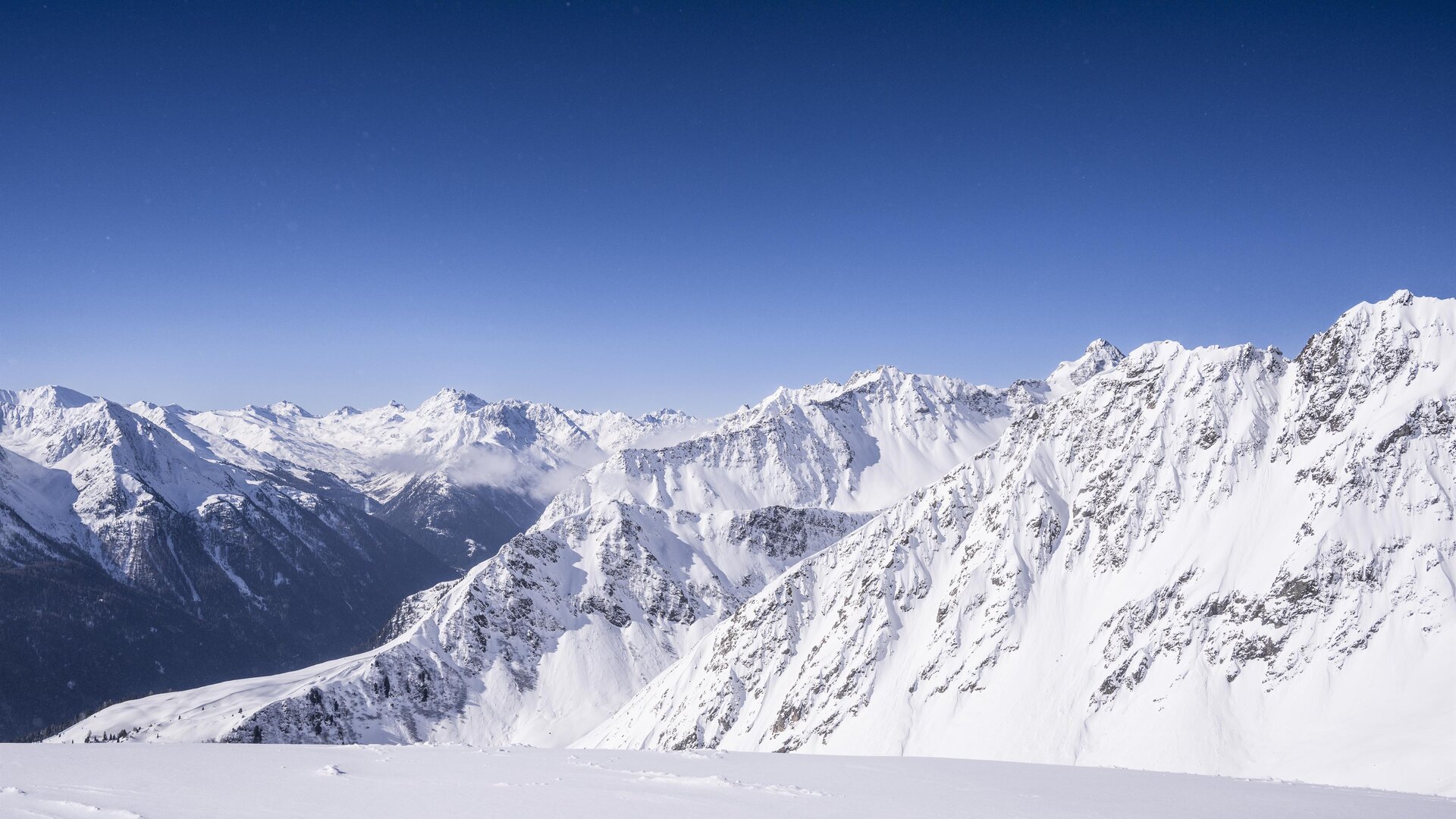 An impressive mountain landscape with snow-covered peaks and clear blue sky. The rugged rocks and deep valleys create a majestic view.
