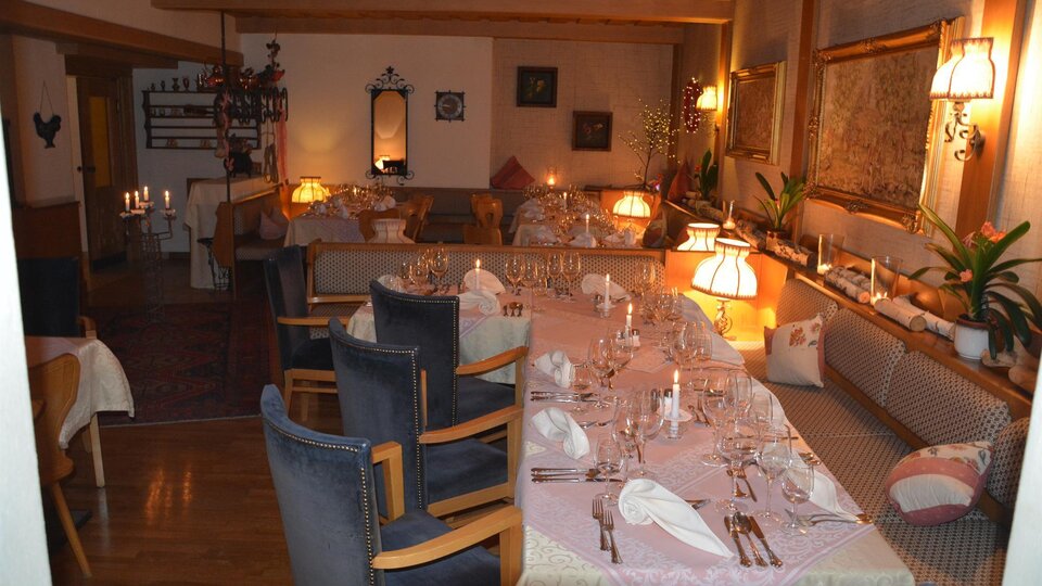 Ein gemütliches Restaurant mit einer langen, gedeckten Tafel und warmem Licht. Die Einrichtung ist einladend und freundlich.