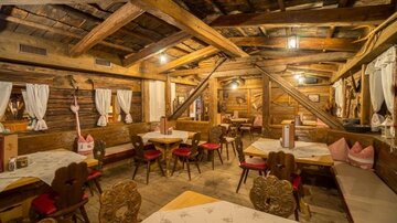 Ein gemütliches Restaurant mit Holzwänden und rustikalen Tischen. Rote Stühle und dekorative Vorhänge schaffen eine einladende Atmosphäre.