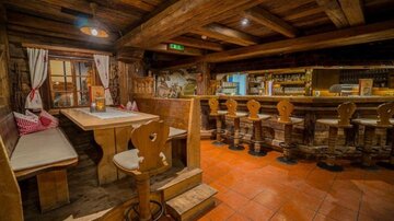 Ein gemütliches Restaurant mit rustikalem Holzinterieur. Die Sitzgelegenheiten bestehen aus Bänken und Hockern an einer Bar.