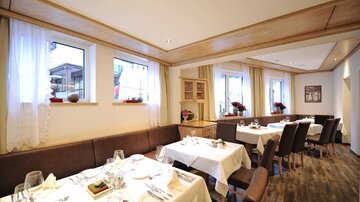 Eine elegante Restaurant-Inneneinrichtung mit weißen Tischdecken und gedeckten Tischen. Große Fenster lassen viel Licht herein und bieten einen Blick auf die Außenumgebung.