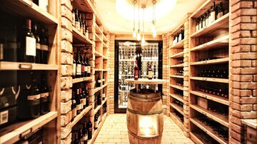 Ein eleganter Weinkeller mit Regalen voller Weinflaschen. In der Mitte steht ein fassförmiges Möbelstück.