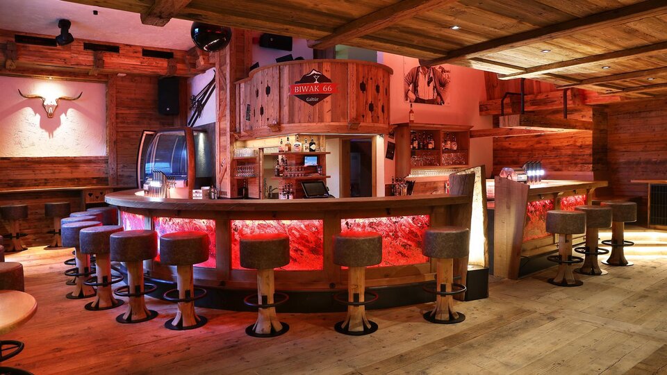 Eine gemütliche Bar mit Holzverkleidung und runden Hockern. Die Beleuchtung sorgt für eine einladende Atmosphäre.