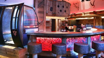 Eine moderne Bar mit einem geschwungenen Tresen und stilvollen Barhockern. Die Innenausstattung ist aus Holz und hat eine lebendige farbige Beleuchtung.