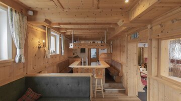 Ein gemütlicher Raum mit Holzverkleidung und großen Fenstern. Es gibt einen langen Tisch und eine Sitzbank, die einladend wirken.