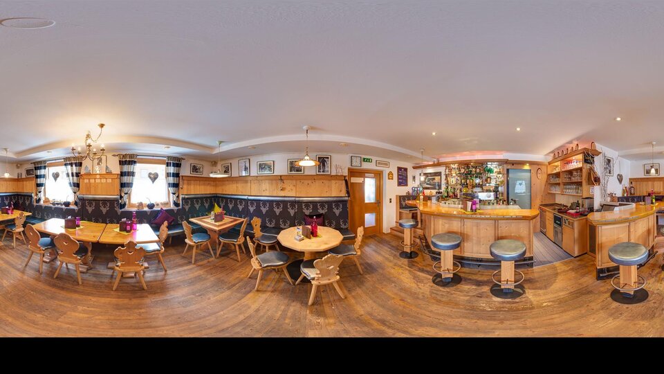 Eine gemütliche Bar mit Holzmöbeln und Tischen. Die Wände sind dekoriert und es gibt eine gut ausgestattete Bar im Hintergrund.