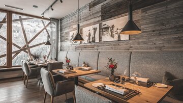 Ein elegantes Restaurant mit holzigen Wänden und gemütlichen Tischen. Große Fenster bieten Ausblick auf die verschneite Landschaft.