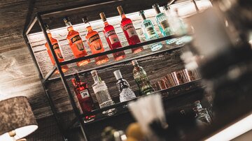 Ein eleganter Barkeeper mit einer Regal voller bunter Spirituosen. Die Flaschen sind sorgfältig angeordnet und schaffen eine einladende Atmosphäre.