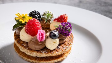 Ein dekoriertes Dessert auf einem weißen Teller. Die Torte besteht aus Waffeln und ist mit verschiedenen Beeren und Sahne verziert.
