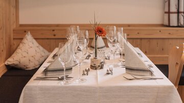 Ein elegant gedeckter Tisch mit Gläsern und dekorierten Servietten. In der Mitte steht eine Blume in einer Vase.