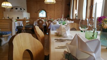 A cozy restaurant with wooden furniture and nicely set tables. The windows let in plenty of daylight, creating an inviting atmosphere.