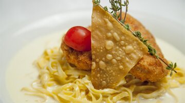 A delicious dish with crispy chicken, served on a bed of noodles in a creamy sauce. Topped with a tomato and a crispy chip.