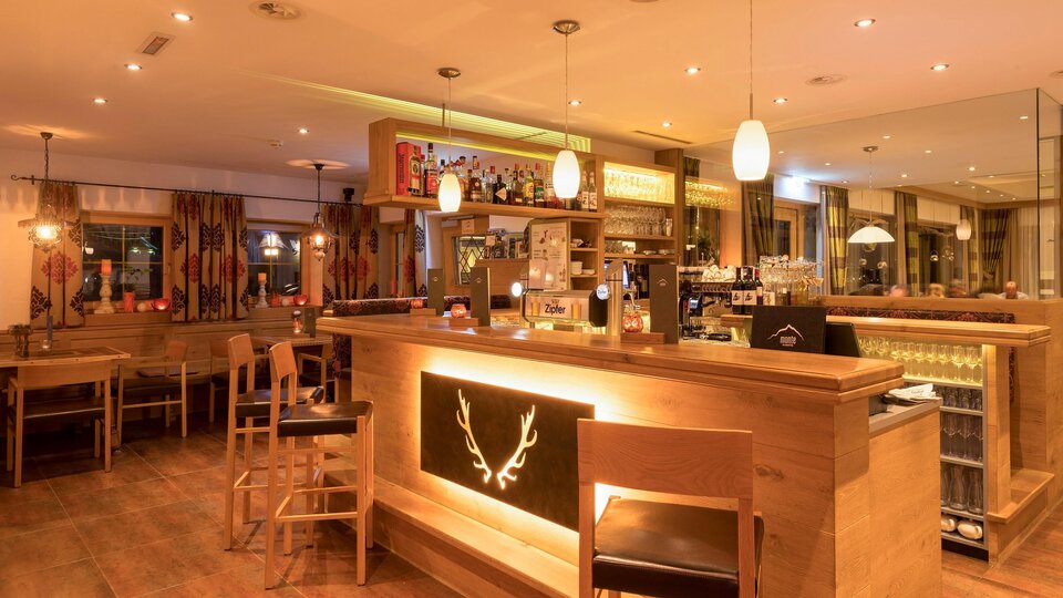 Eine einladende Bar mit Holzmöbeln und gedämpfter Beleuchtung. Im Hintergrund sind Theken und Regale mit Getränken zu sehen.