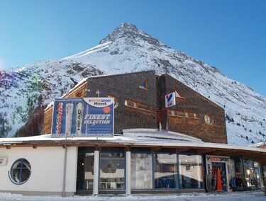 A modern building in front of a snow-covered mountain. The clear sky and winter landscape create a picturesque view.
