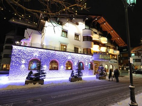 Ein charmantes Hotel in einer verschneiten Stadt bei Nacht. Die Fassade ist mit bunten Lichtern beleuchtet und sorgt für eine festliche Stimmung.