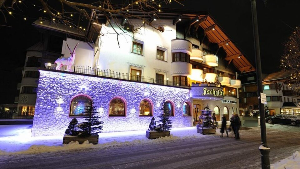 Ein charmantes Hotel in einer verschneiten Stadt bei Nacht. Die Fassade ist mit bunten Lichtern beleuchtet und sorgt für eine festliche Stimmung.
