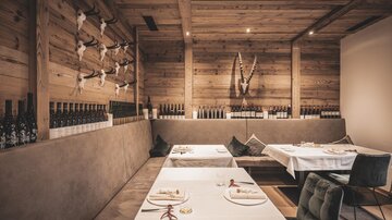 Ein modernes Restaurant mit Holzwänden und eleganten Tischen. An der Wand sind Flaschen und dekorative Elemente aus Naturmaterialien zu sehen.