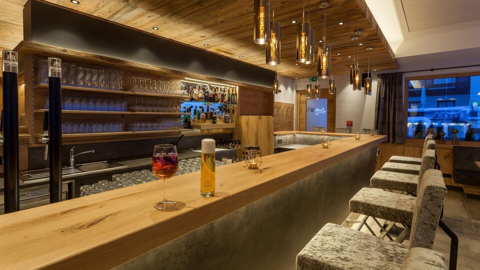 Eine moderne Bar mit Holzdekor und eleganten Leuchten. Im Hintergrund befinden sich Gläser und eine Auswahl an Getränken.
