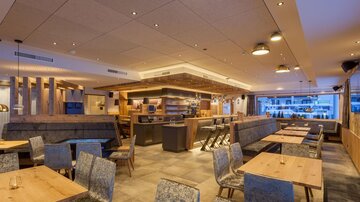 Ein modernes Restaurant mit Holzdetails und gemütlichen Tischen. Die Beleuchtung sorgt für eine einladende Atmosphäre.