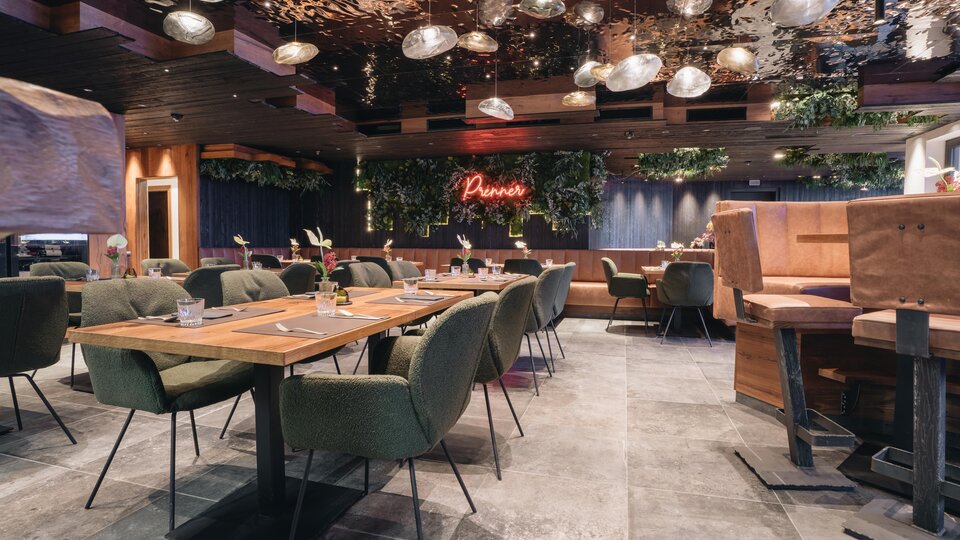 Ein modernes Restaurant mit gemütlichen Tischen und stilvollen Stühlen. Die Beleuchtung und Pflanzen schaffen eine einladende Atmosphäre.