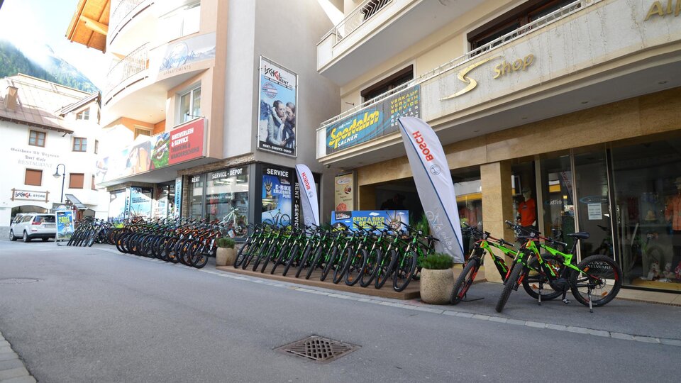 A street with several bicycles available for rent. In the background, shops and advertising flags are visible.