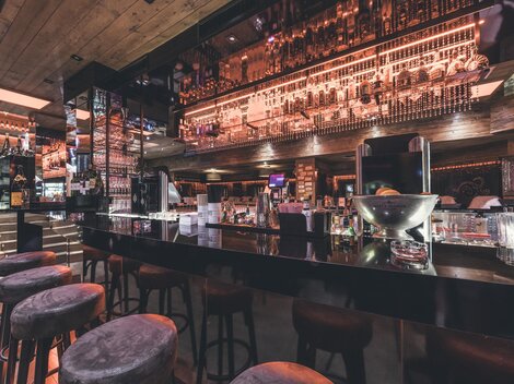 Eine moderne Bar mit einer eleganten Theke und stilvollen Barhockern. Die Beleuchtung und Dekoration schaffen eine einladende Atmosphäre.