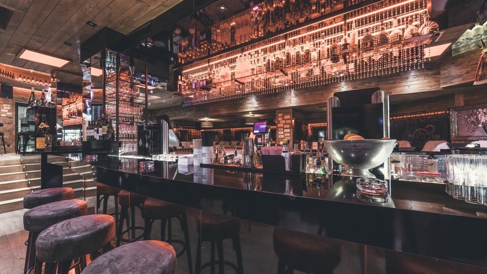 Eine moderne Bar mit einer eleganten Theke und stilvollen Barhockern. Die Beleuchtung und Dekoration schaffen eine einladende Atmosphäre.