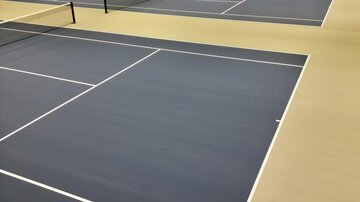 A modern tennis hall with several playing courts. The blue courts are well-lit and ready for play.