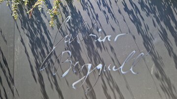 Eine schwarze Tafel mit eleganter Schrift. Die Namensinschrift ist von Schatten umgeben.