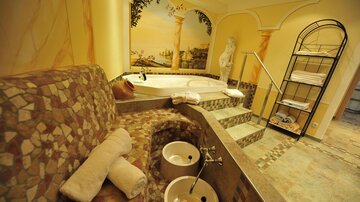 Ein elegantes Spa mit einem runden Whirlpool und einer gemütlichen Sitzecke. Die Wände sind kunstvoll bemalt und vermitteln eine entspannende Atmosphäre.
