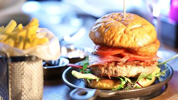 Ein saftiger Burger mit Tomaten und Salat in einem knusprigen Brötchen. Dazu gibt es eine Portion Pommes frites.