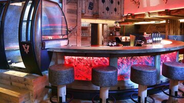 Eine moderne Bar mit Holzdesign und gemütlichen Sitzplätzen. Die Atmosphäre wird durch farbige Beleuchtung hervorgehoben.