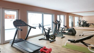 Ein modernes Fitnessstudio mit verschiedenen Trainingsgeräten. Große Fenster bieten viel Tageslicht und eine angenehme Atmosphäre.