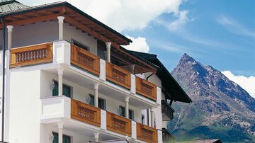Ein modernes Gebäude mit Balkonen aus Holz und einer schönen Berglandschaft im Hintergrund. Der Himmel ist klar und die Umgebung ist malerisch.