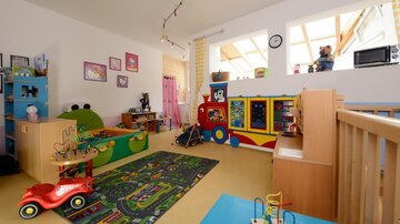 Ein buntes Kinderzimmer mit Spielzeug, einem Teppich und einem Spielbereich. Es gibt eine Spielecke mit einem Spielzeugbus und einem roten Auto.