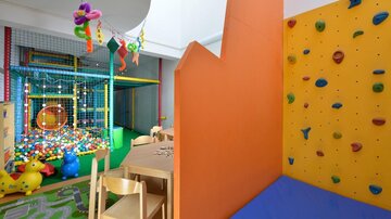 Ein bunter Spielplatz für Kinder mit einem Bällebad und einer Kletterwand. Es gibt auch Spieltische und bunte Wandflächen.