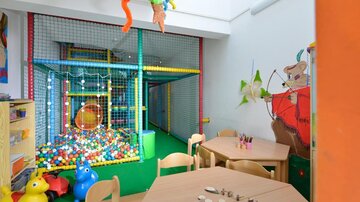 Ein heller Spielraum mit einem bunten Bällebad und einem Spielturm. Rund um die Tische stehen bunte Spielzeuge und Malutensilien.