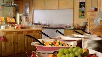 Ein buntes Buffet mit frischem Obst in Schalen. Im Hintergrund ist eine gemütliche Gastronomie-Umgebung zu sehen.