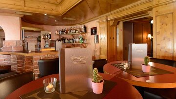 Ein stilvolles Restaurant mit Holzwänden und runden Tischen. Auf den Tischen stehen kleine Pflanzen und Menükarten.