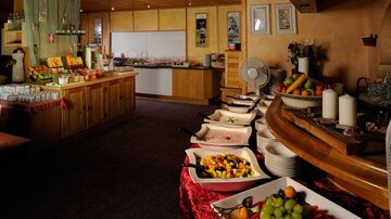 Ein einladender Frühstücksraum mit einem Buffet voller frischer Früchte. Im Hintergrund sind verschiedene Speisen und Getränke auf Holzmöbeln angerichtet.
