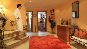 Ein stilvolles Spa mit warmen Farben und bequemer Einrichtung. Eine Person in einem Bademantel steht auf der Treppe und genießt die entspannende Atmosphäre.
