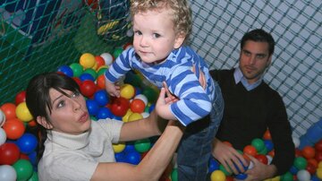 Ein kleiner Junge steht in einem Bällebad, während eine Frau ihn anhebt. Ein Mann sitzt daneben und beobachtet die Situation.