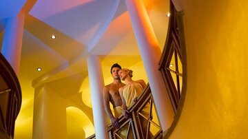 Ein Paar steht auf einer eleganten Treppe mit weichem Licht in warmen Farben. Die Atmosphäre ist romantisch und einladend.