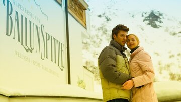 Ein Paar steht vor einem Gebäude im Schnee, das den Namen "BallunSpitze" trägt. Die beiden wirken glücklich und genießen die winterliche Atmosphäre.
